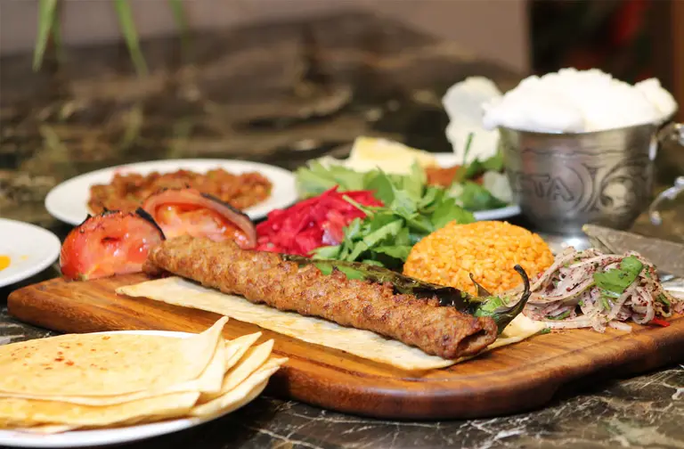 Tahtada lavaş üstünde Adana kebap, köz domates ve bulgur pilavı